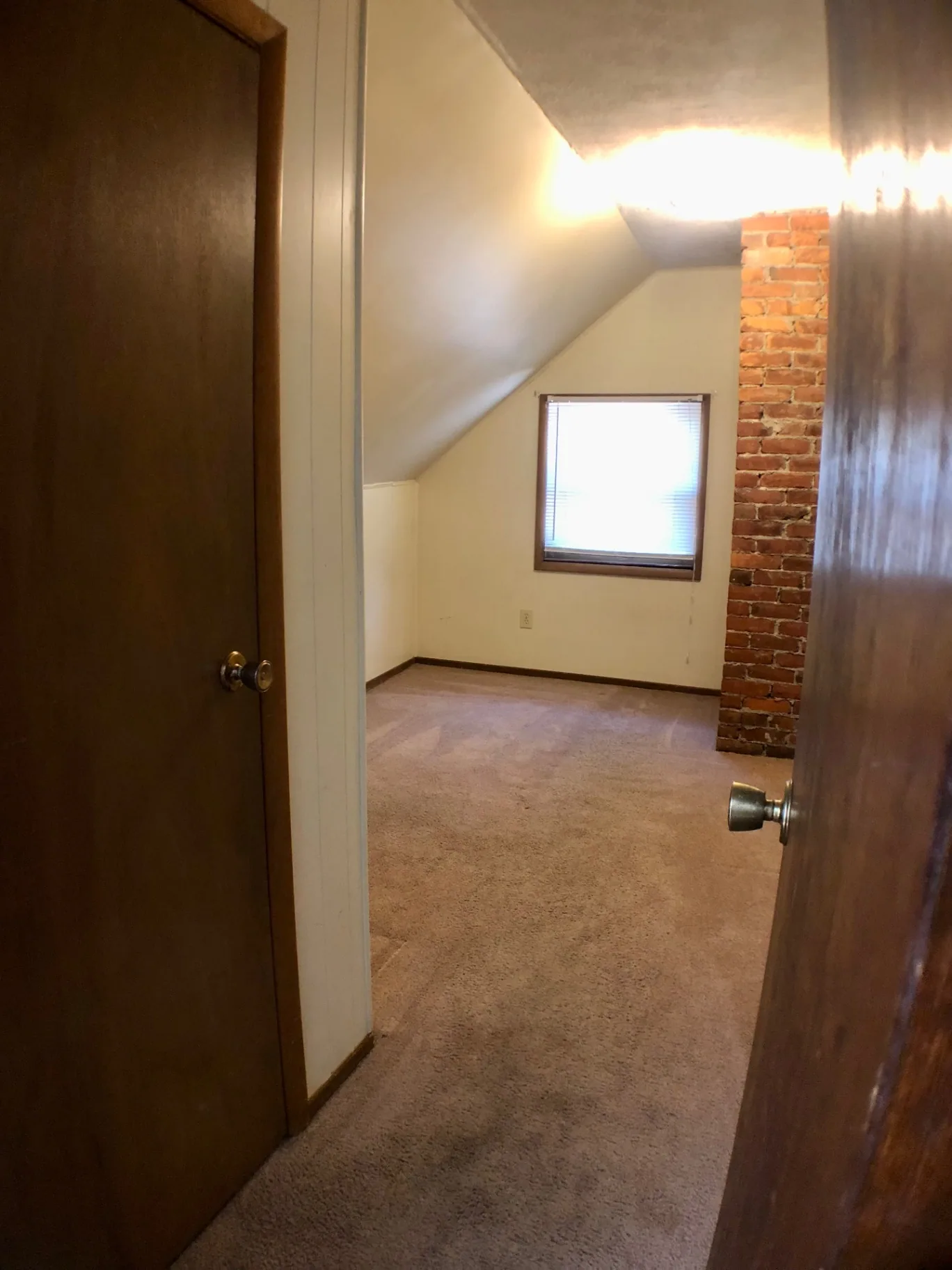 Carpeted bedroom with sloped ceiling, exposed brick chimney, and window