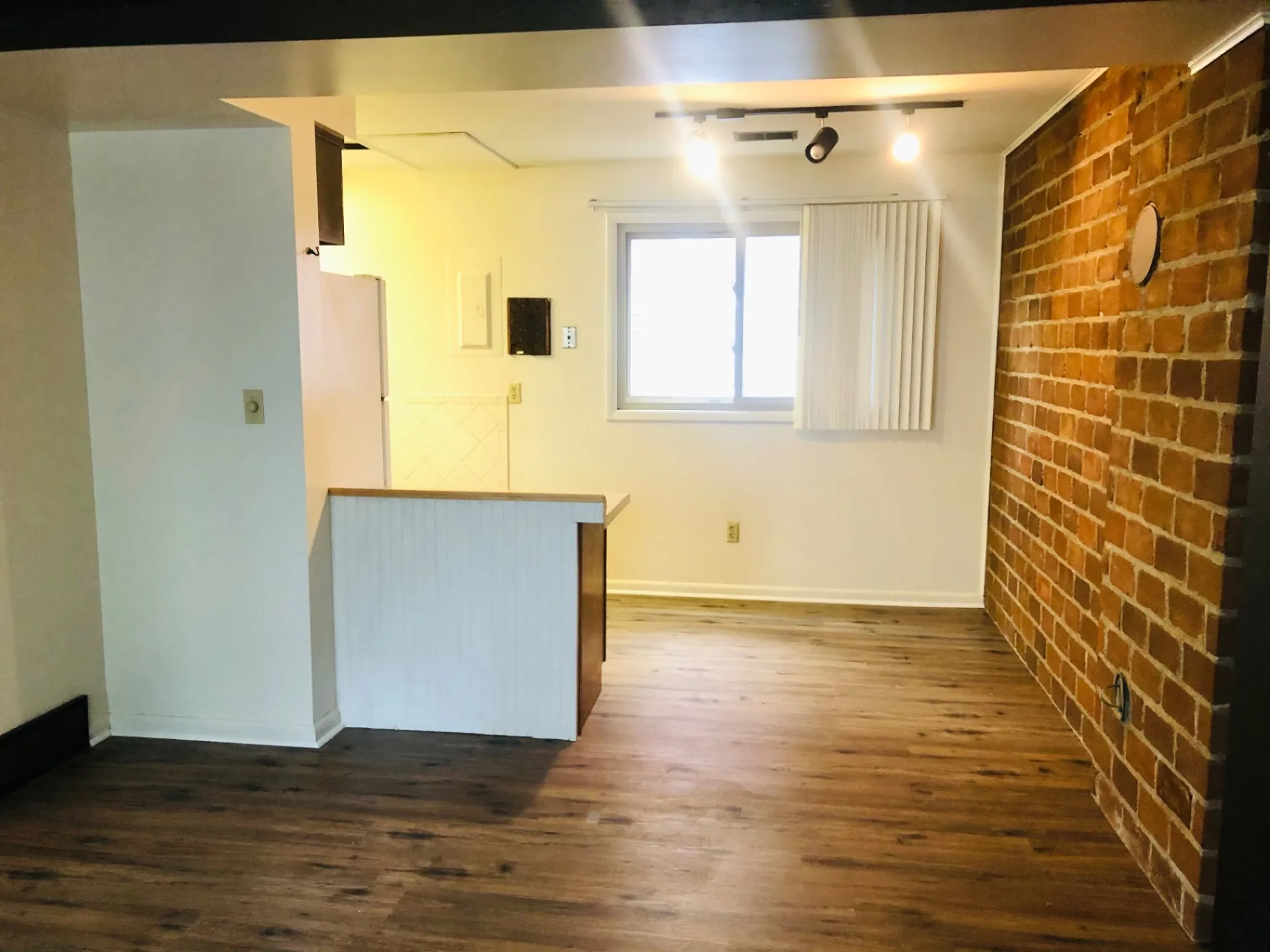2011 Summit St. Unit B open dining/living area with exposed red brick accent wall, plank floors, and kitchen pass-through