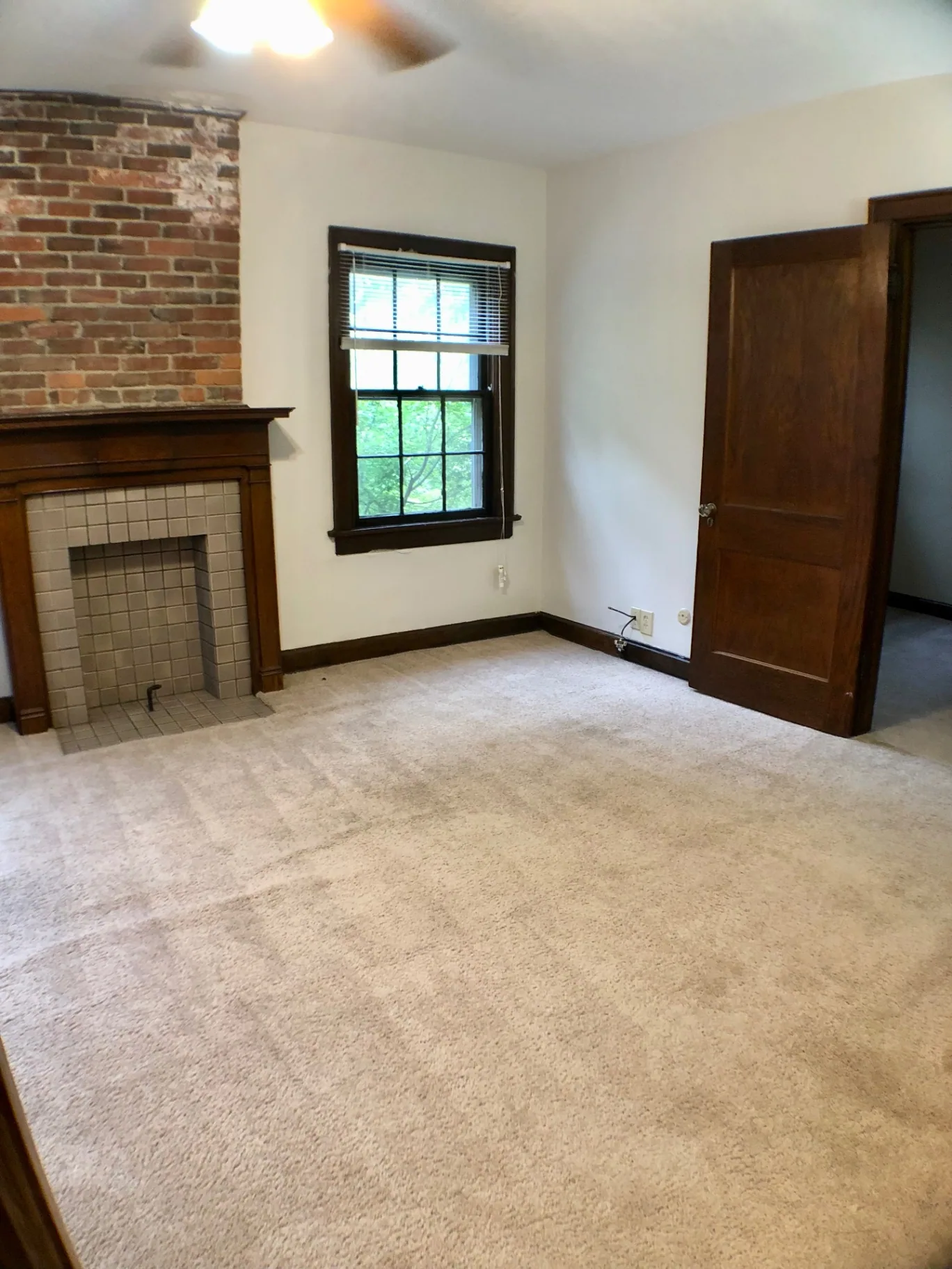 2054 Iuka Ave. D living room angle showing tile fireplace, ceiling fan, exposed brick, and original wood doors