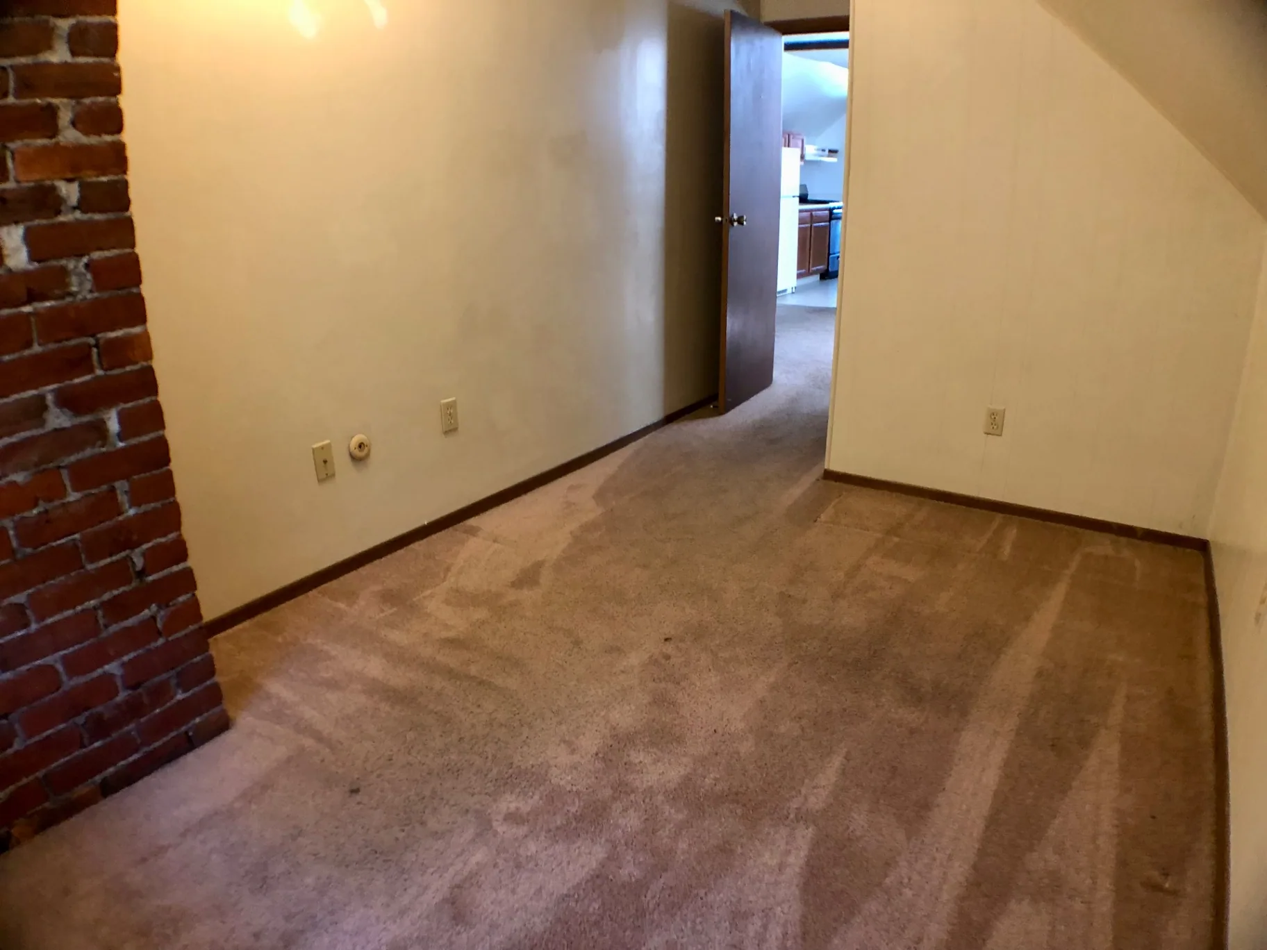 Empty bedroom with exposed brick accent wall and sloped ceiling