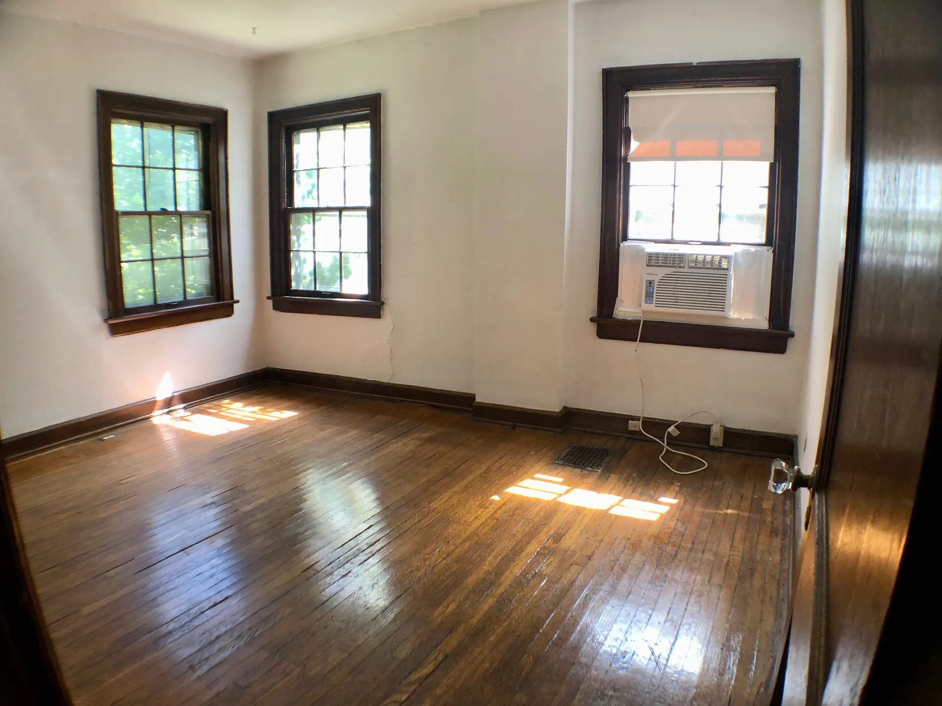 2044 Iuka Ave. A bright bedroom with three wood-trim windows, hardwood floors, and window AC