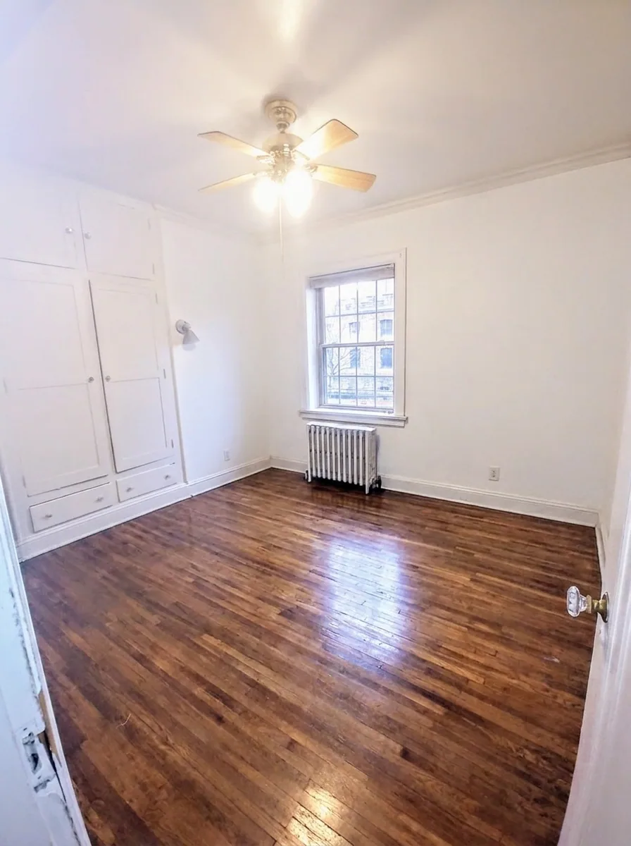 Unit B bedroom with built-in white cabinets, ceiling fan, and large window