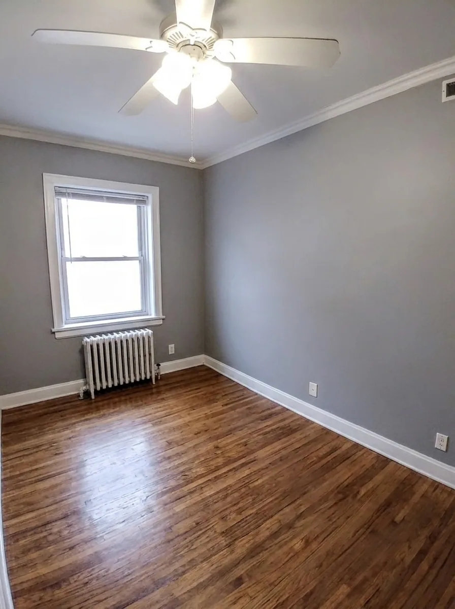 Unit B bedroom with gray walls, hardwood floors, ceiling fan, and radiator under window