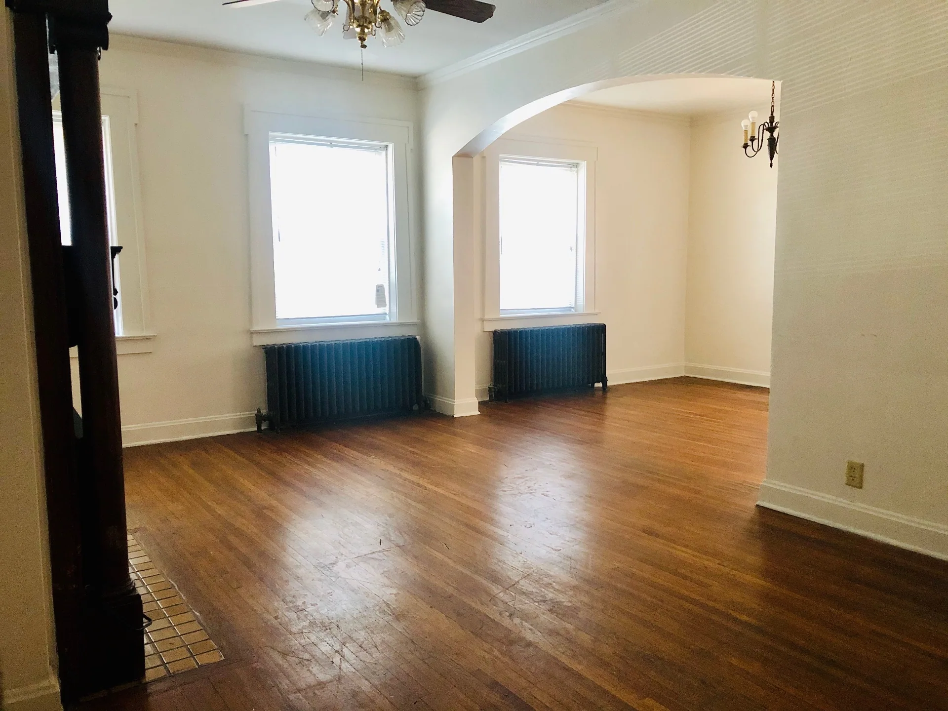Unit G wide living and dining room with arched opening, hardwood floors, and twin radiators