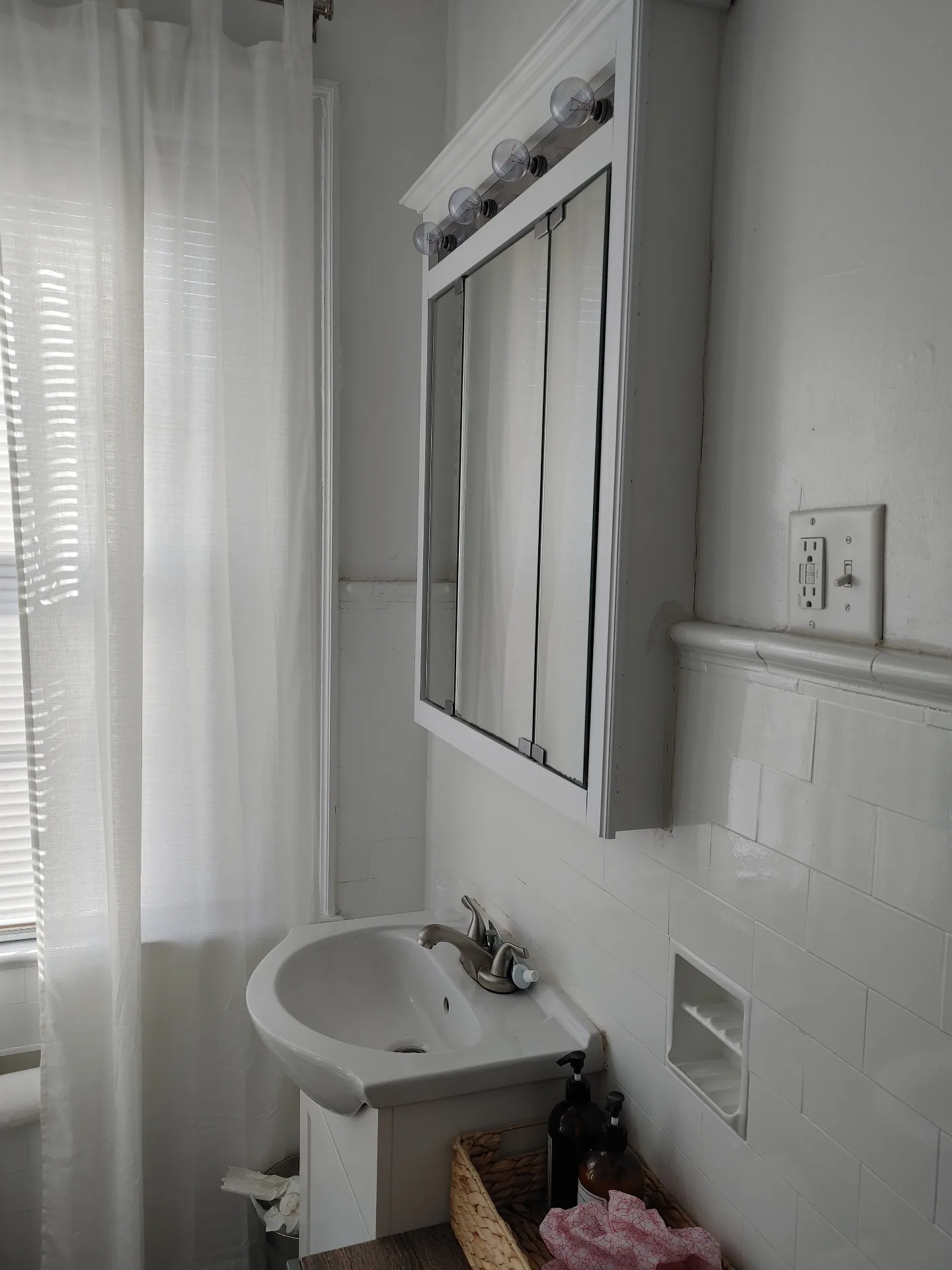 Unit G bathroom sink and mirrored medicine cabinet beside the shower curtain