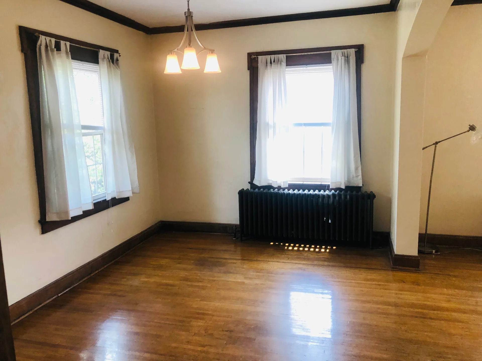 Unit K dining area with large windows, curtains, cast iron radiator, and hardwood floors