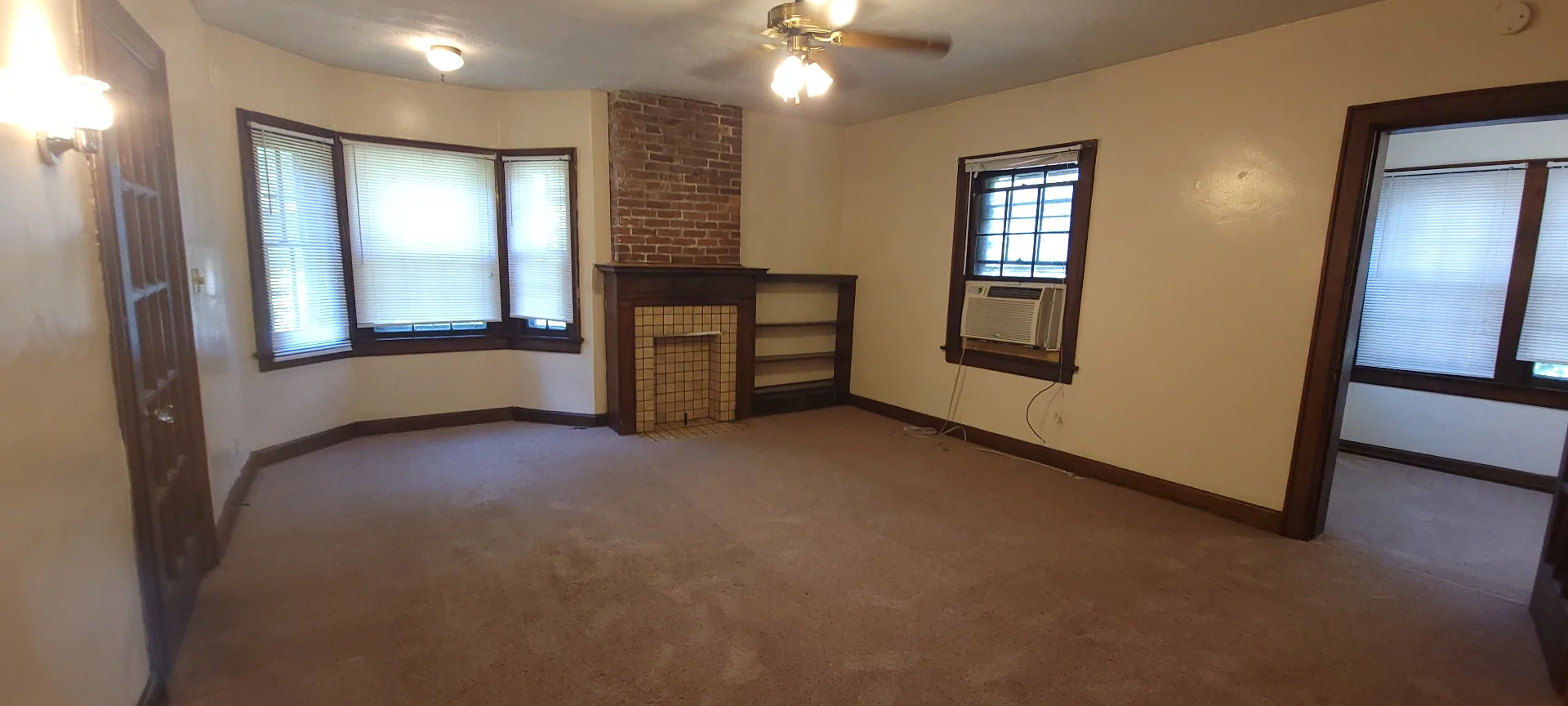 2054 Iuka Ave. C wide living room view with brick fireplace, bay window, ceiling fan, and built-in shelving