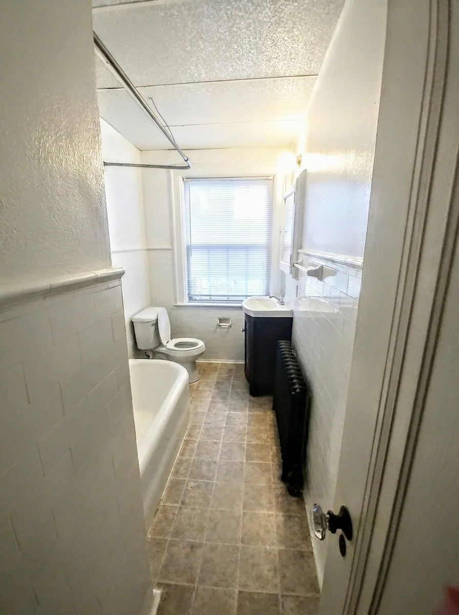 Unit I bathroom with tub, vanity, radiator, and tiled floor