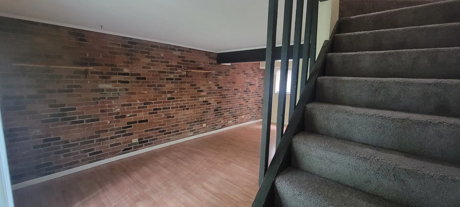 2022 Iuka Ave. open living area with exposed brick accent wall, plank flooring, and carpeted staircase