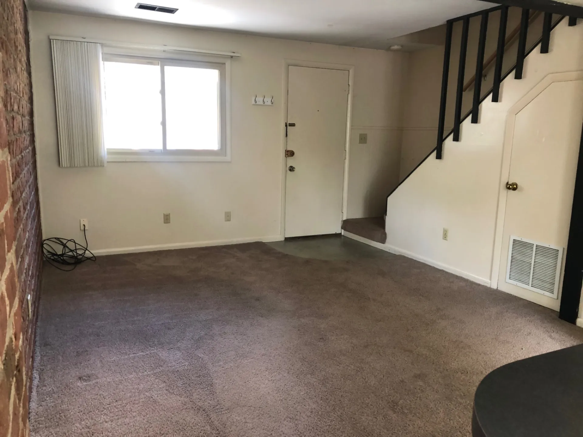 2011 Summit St. Unit F open living room with wood-look plank floors, exposed brick, and staircase with black railing