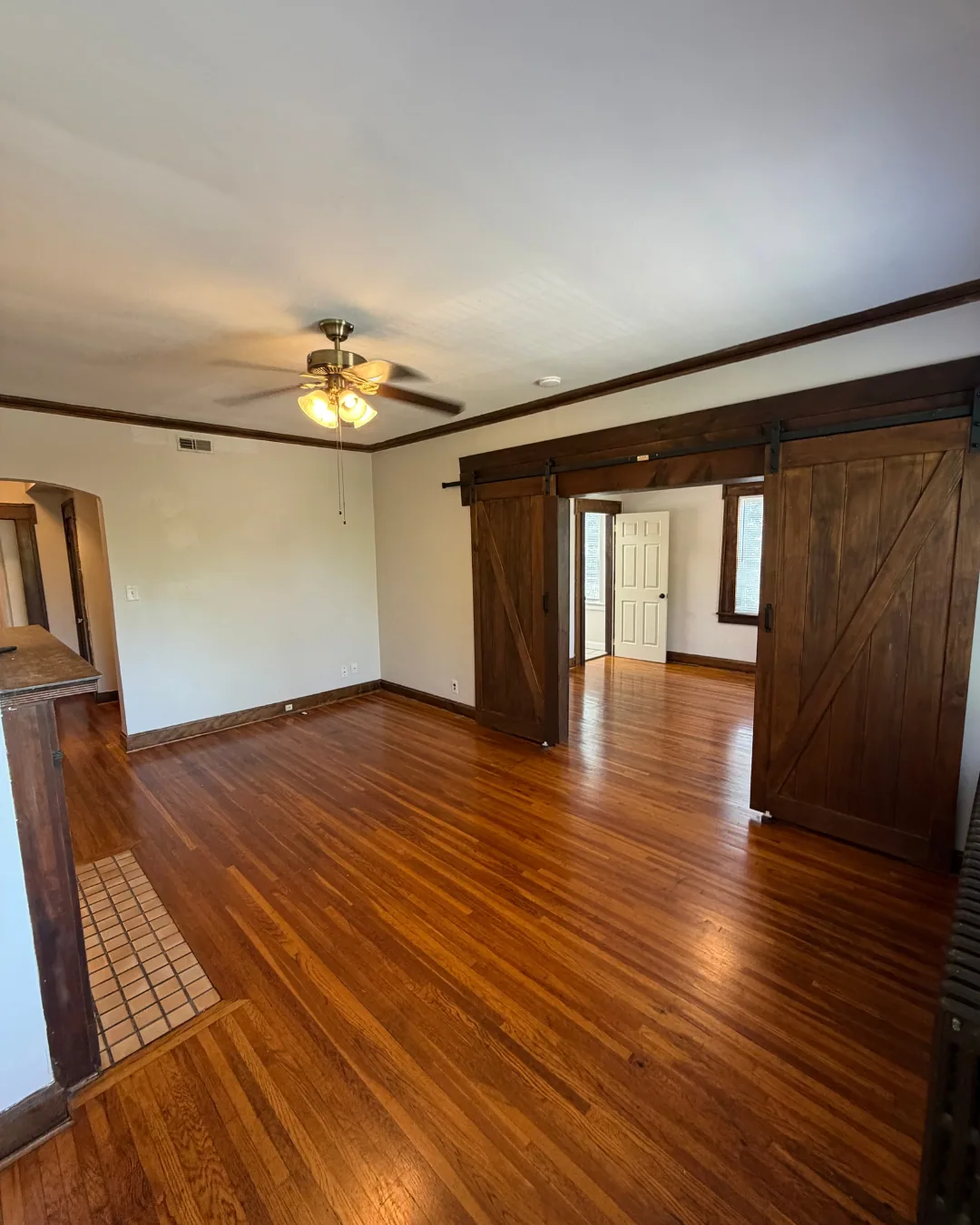 Open living area with barn doors, ceiling fan, and hardwood floors