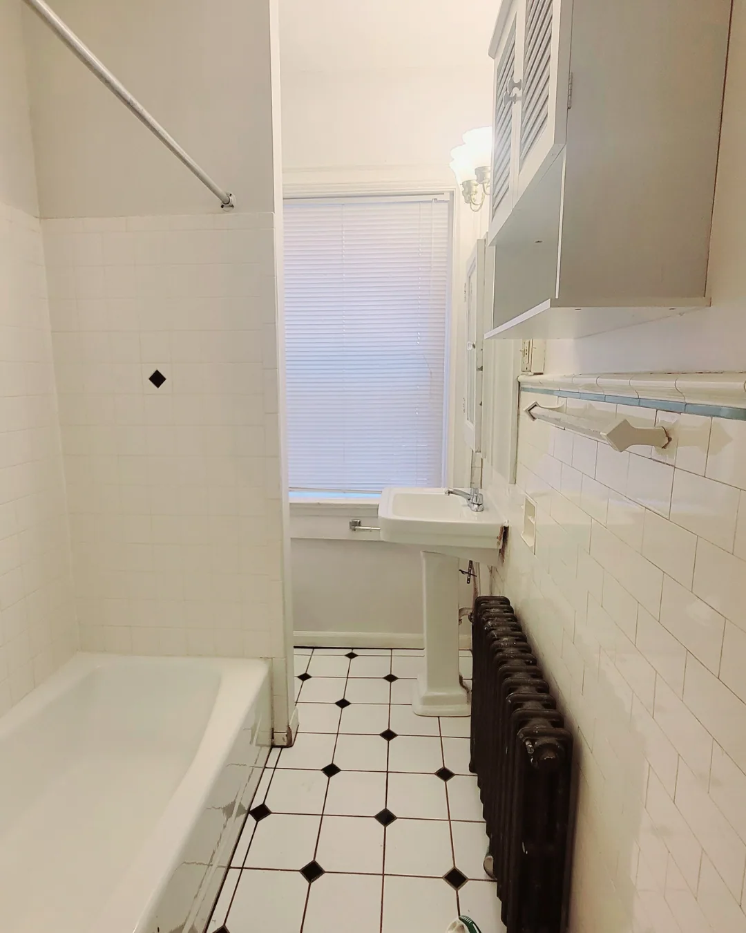 Unit A bathroom with pedestal sink, tub, radiator, and white tile floor