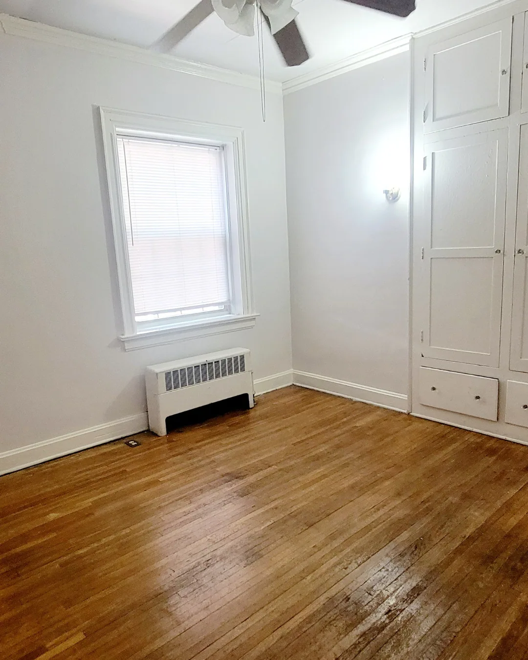Unit A bedroom with hardwood floors, built-in storage, and window radiator
