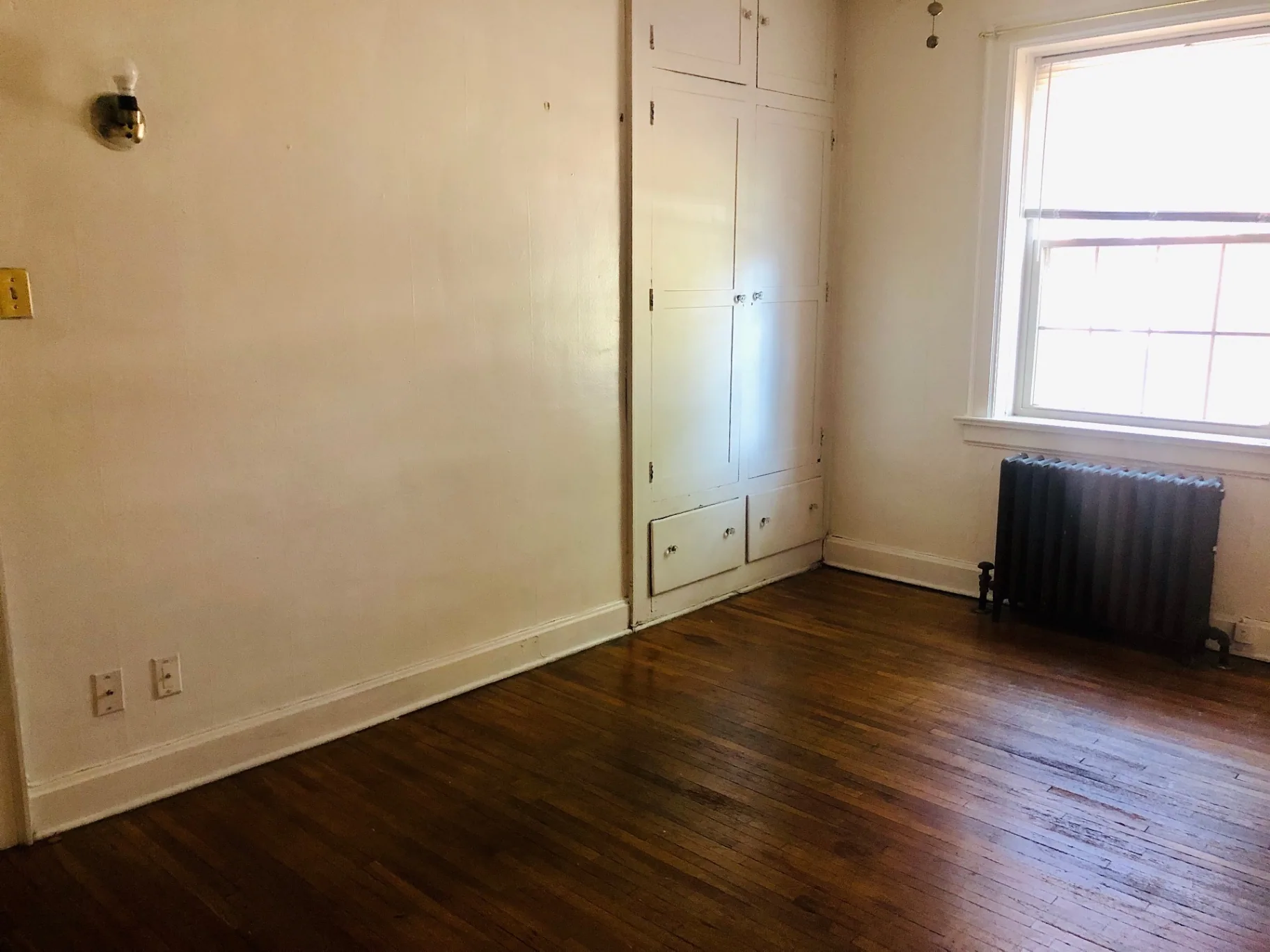 Unit G bedroom with built-in closet, cast iron radiator, and hardwood floors