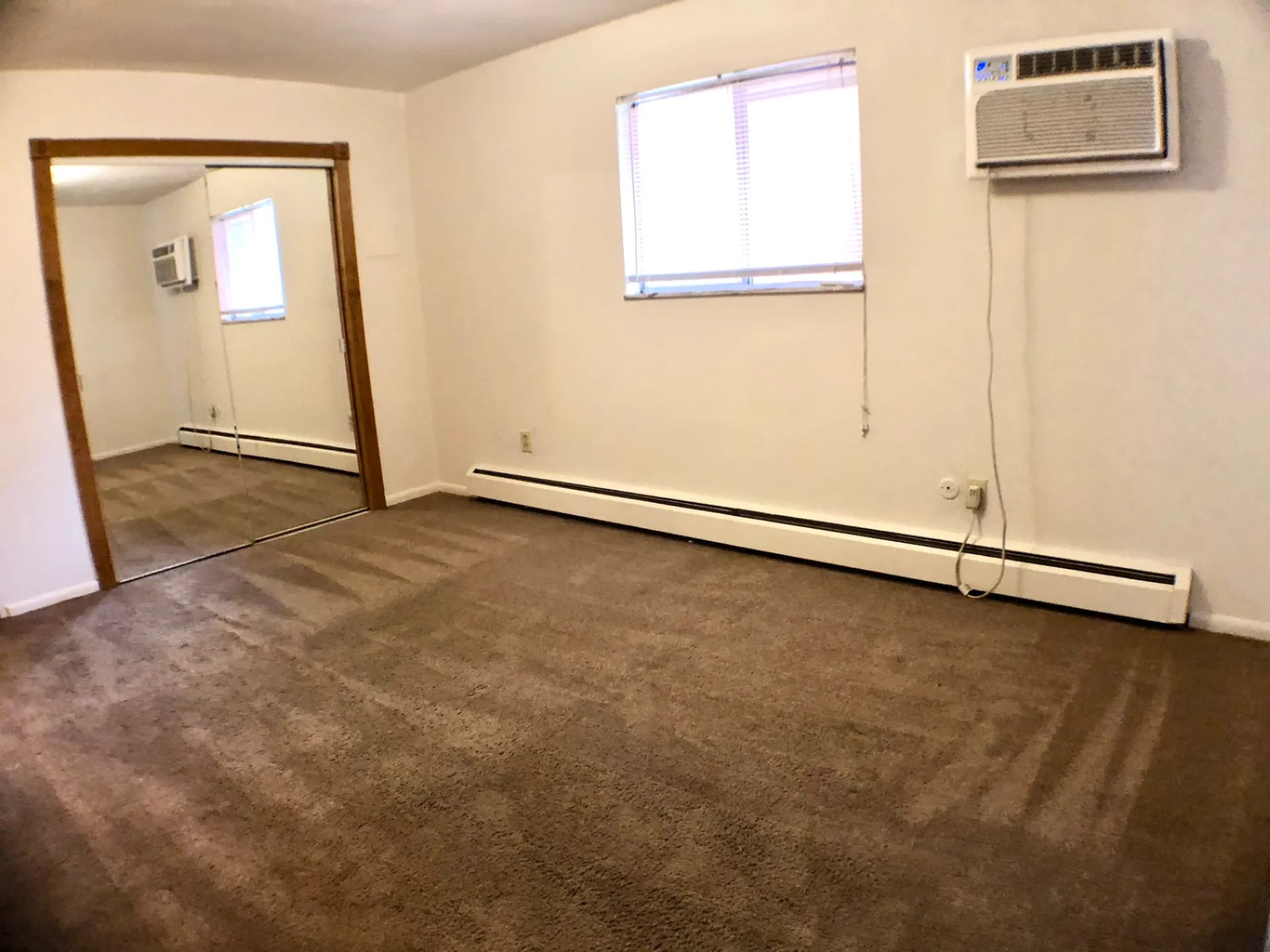 1827 N 4th St. Unit 4 carpeted bedroom with mirrored closet doors, window AC, and baseboard heat