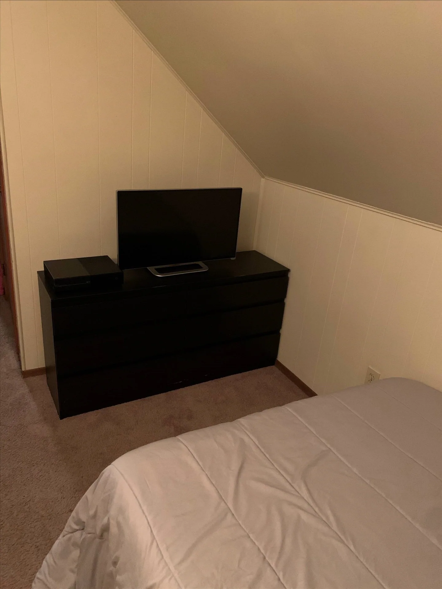 Furnished bedroom nook with dresser and TV under a sloped ceiling