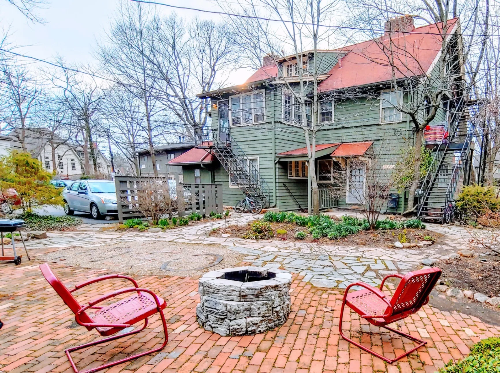 Wide view of shared brick courtyard with fire pit, red chairs, and green building