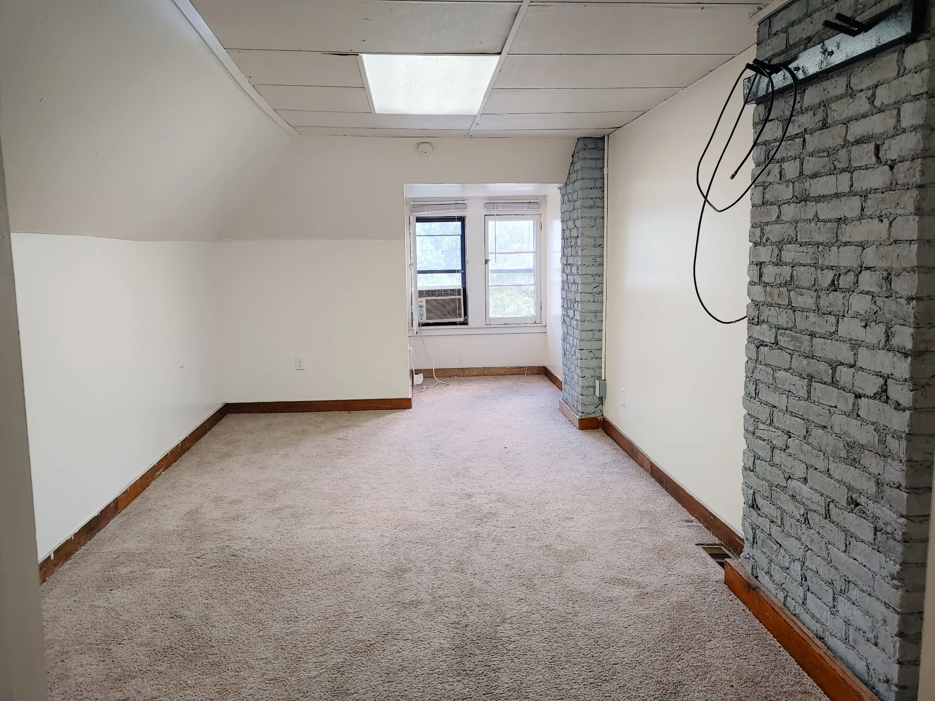89 E Woodruff Ave. Unit C living area with window AC, exposed brick, and plush neutral carpet
