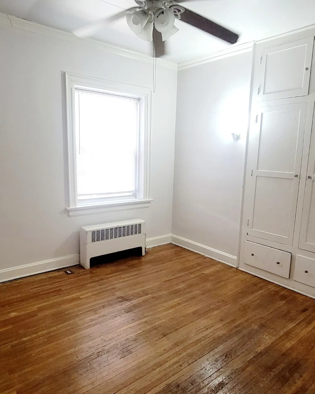 Unit A bedroom with hardwood floors, built-in cabinets, and ceiling fan
