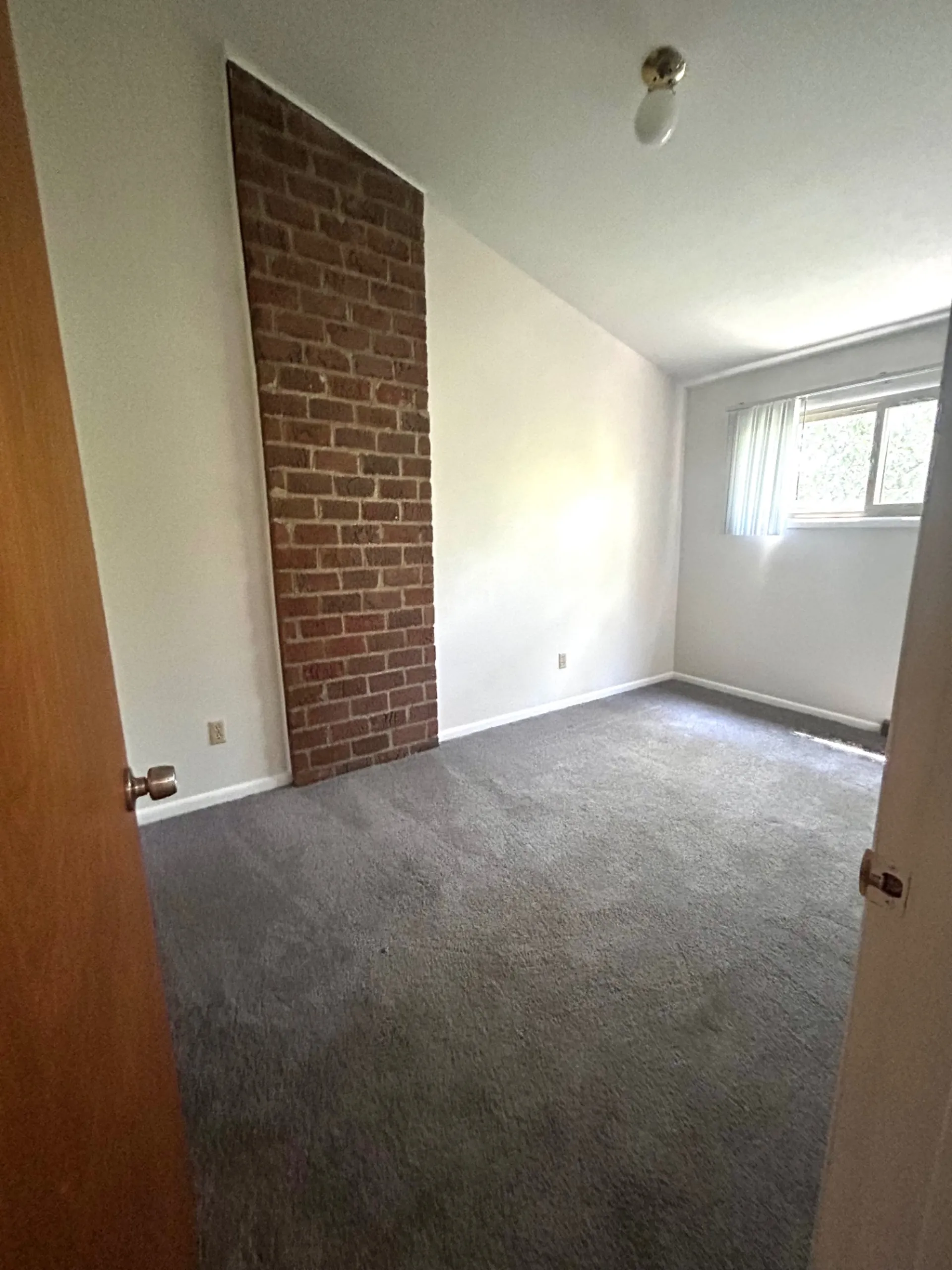 2011 Summit St. Unit E second bedroom with exposed brick accent wall and gray carpet