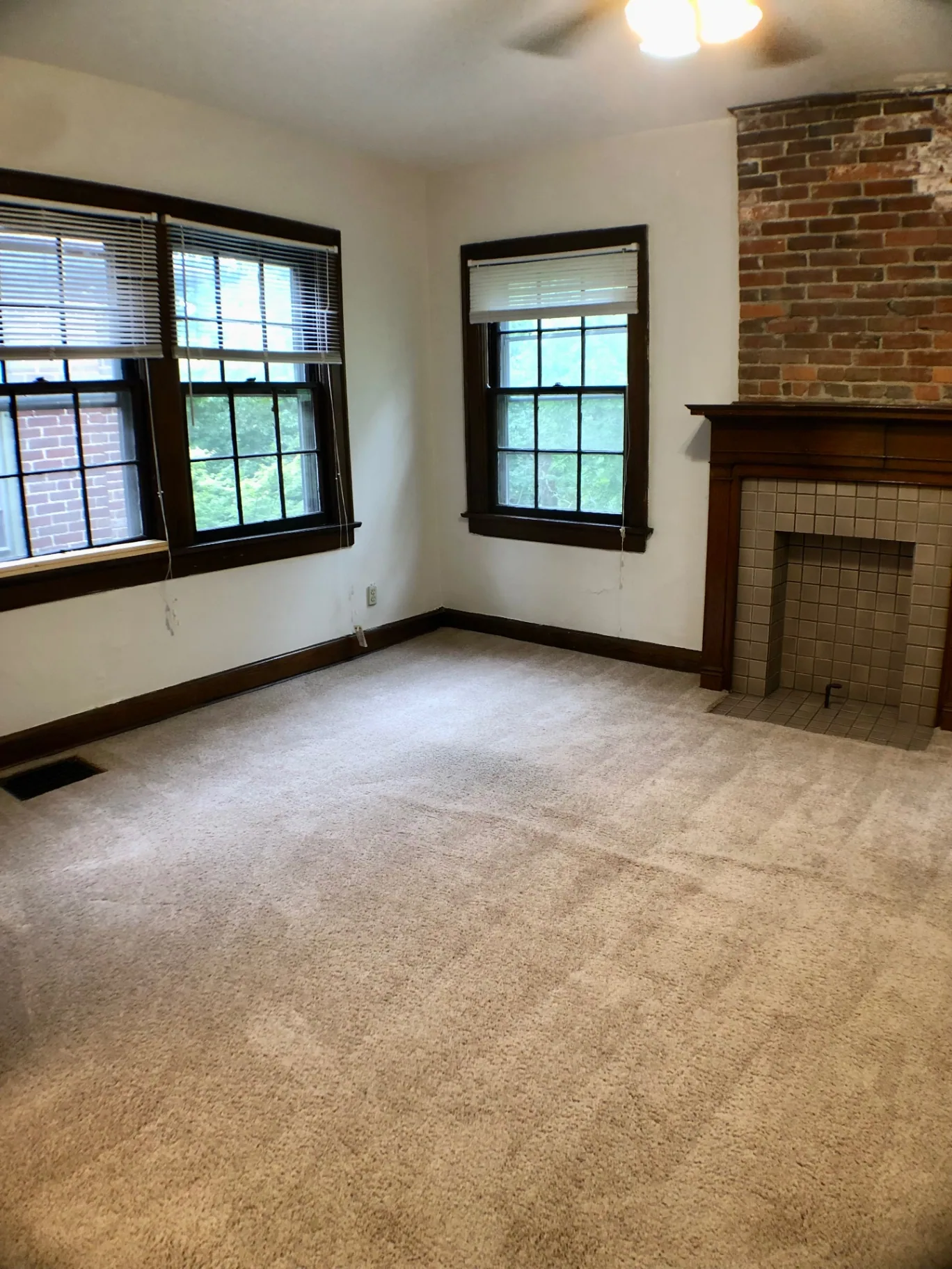 2054 Iuka Ave. D living area with tile fireplace, exposed brick, three windows, and ceiling fan