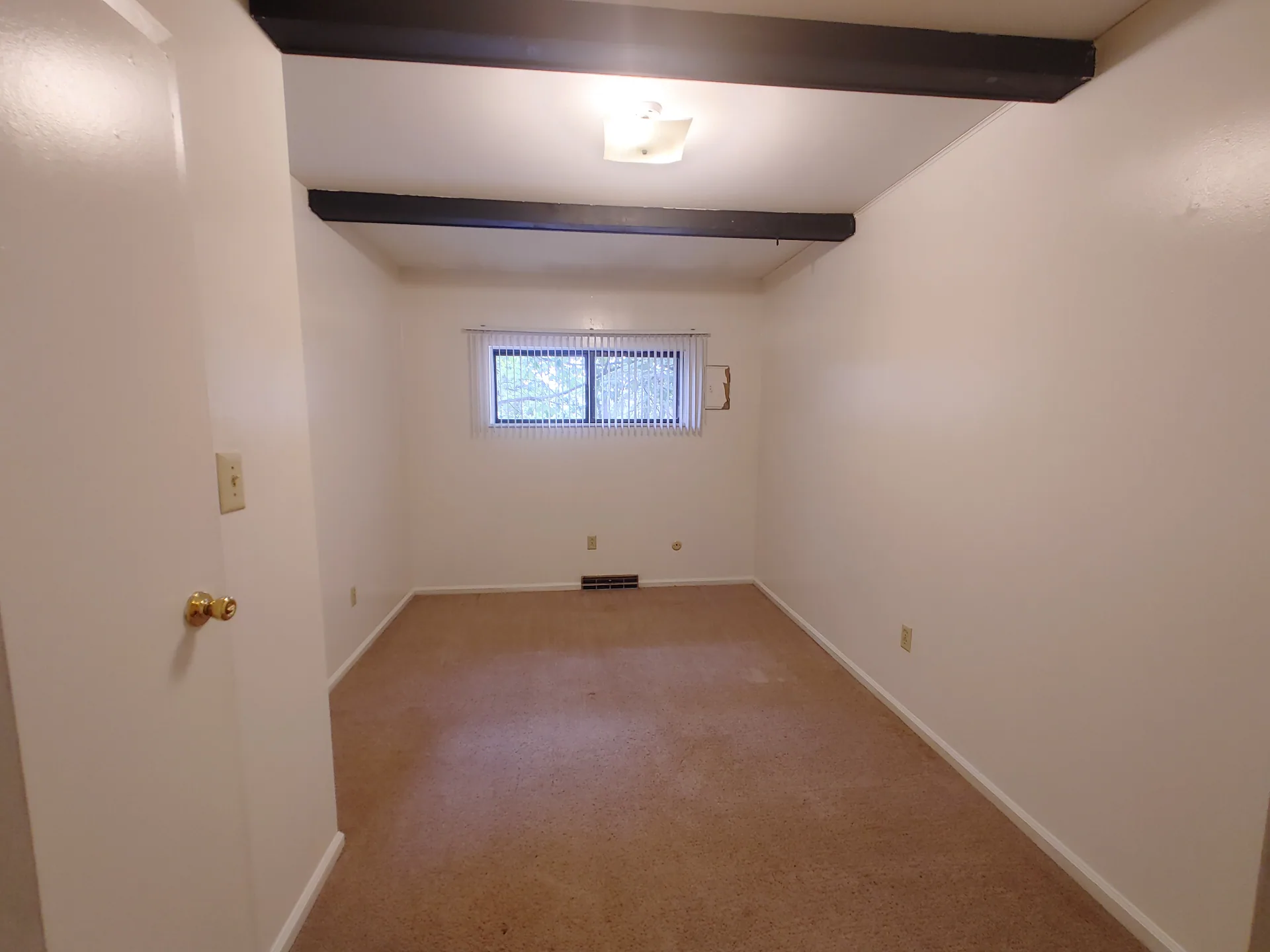 2020 Iuka Ave. bedroom with dark ceiling beams, fresh carpet, and a window overlooking trees