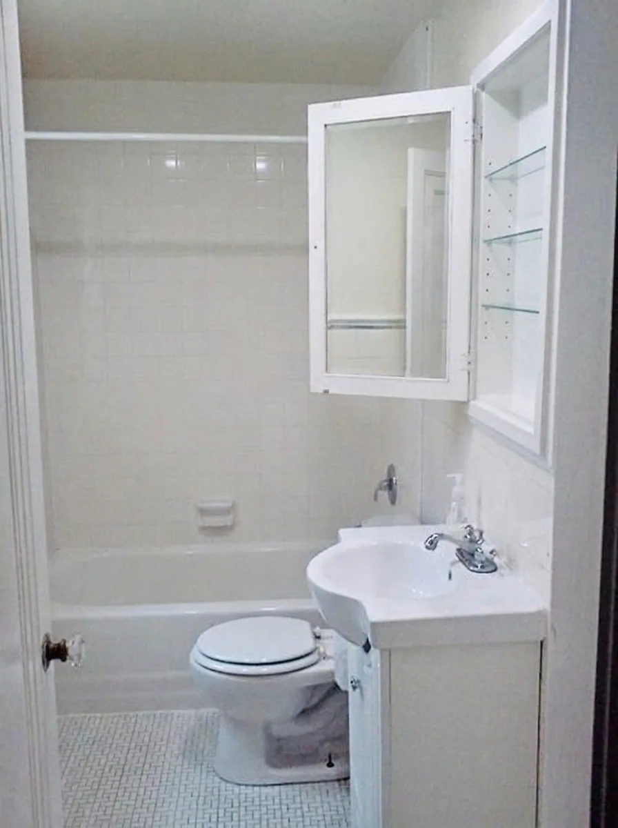 Unit D white tiled bathroom with tub, pedestal sink, and medicine cabinet