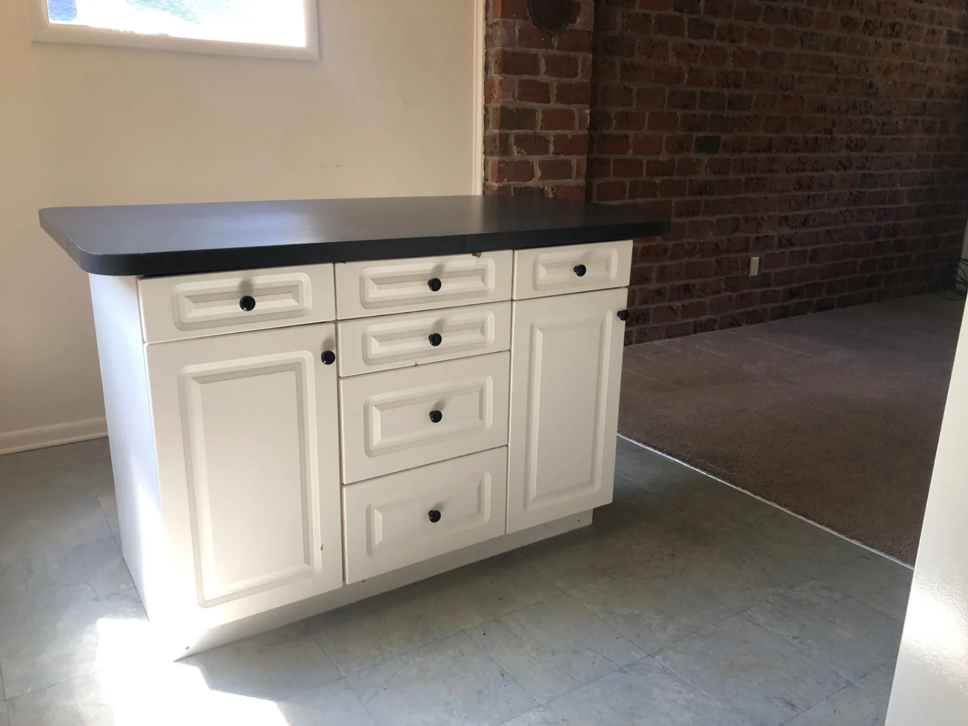 2011 Summit St. Unit F kitchen island with white cabinets, black countertops, and exposed brick backdrop