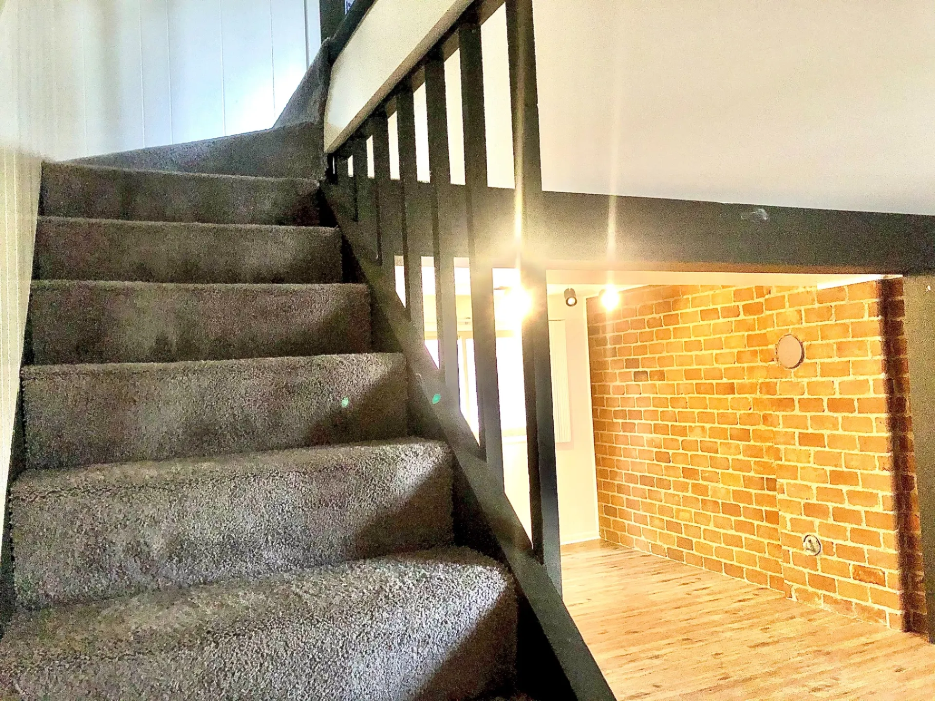 2011 Summit St. Unit B carpeted staircase with black railing and exposed brick accent wall