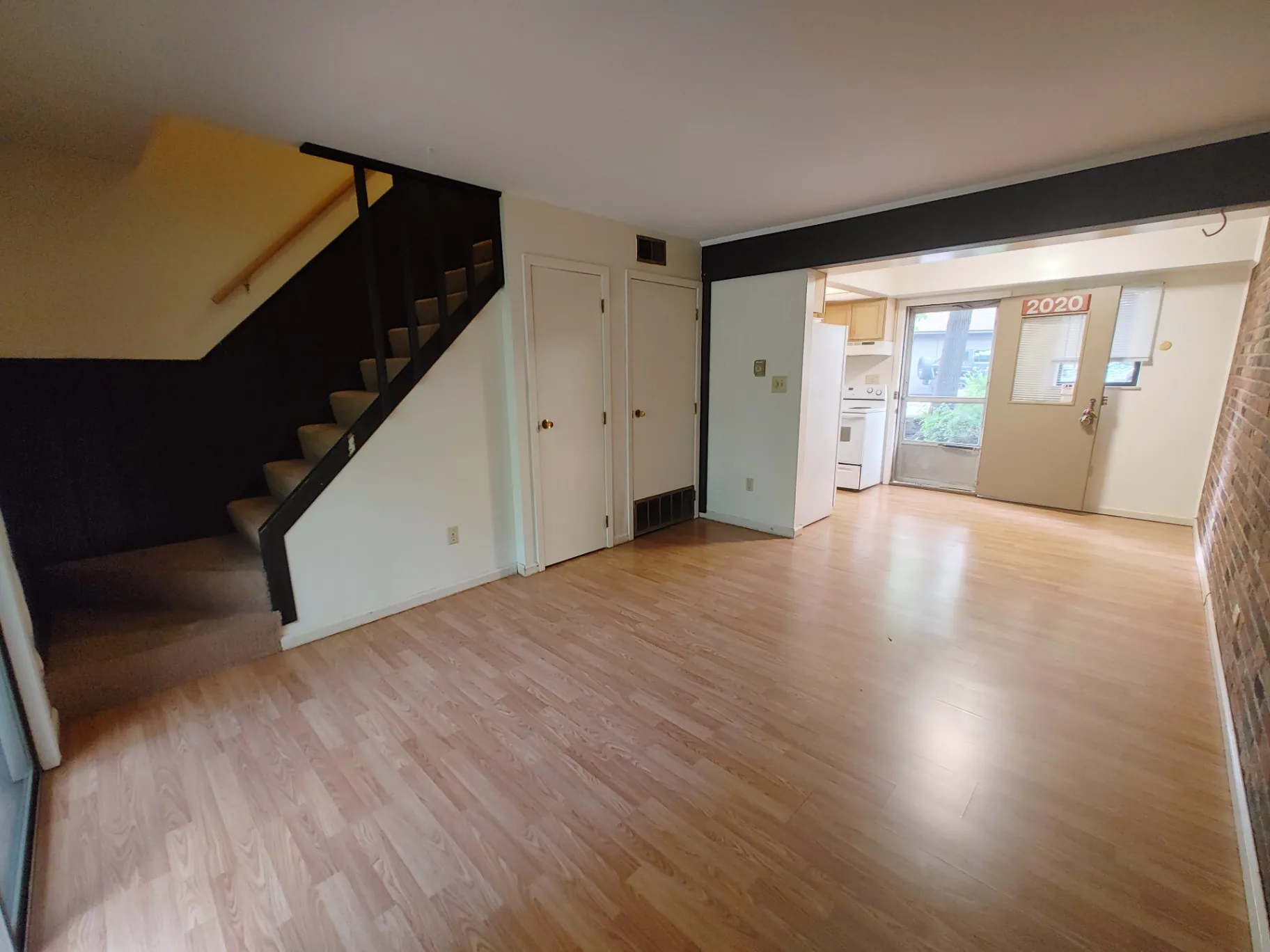 2020 Iuka Ave. open living room with staircase, wood-look floors, exposed brick wall, and front door labeled 2020