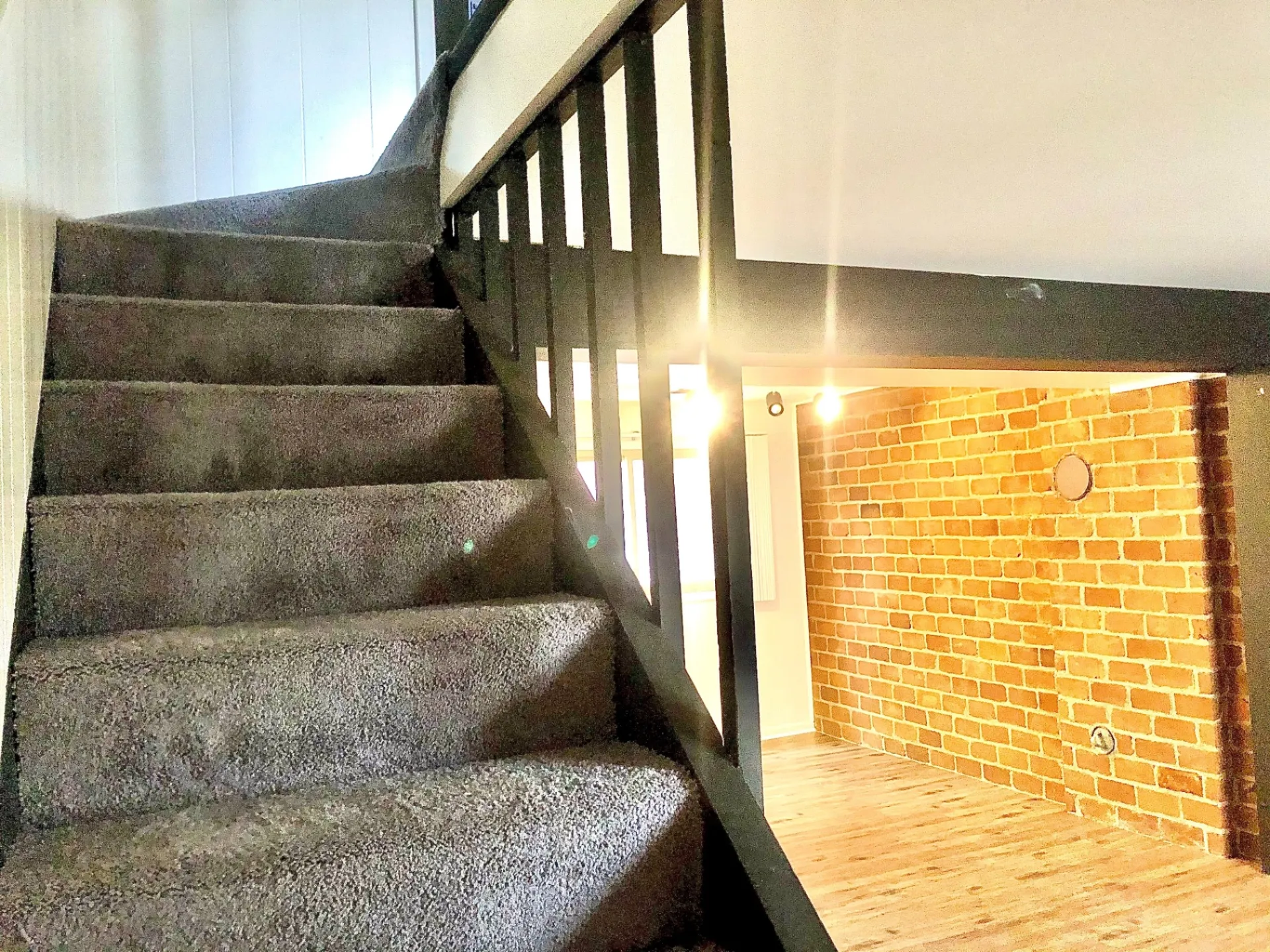 2011 Summit St. Unit D carpeted staircase with black railing and exposed brick accent wall