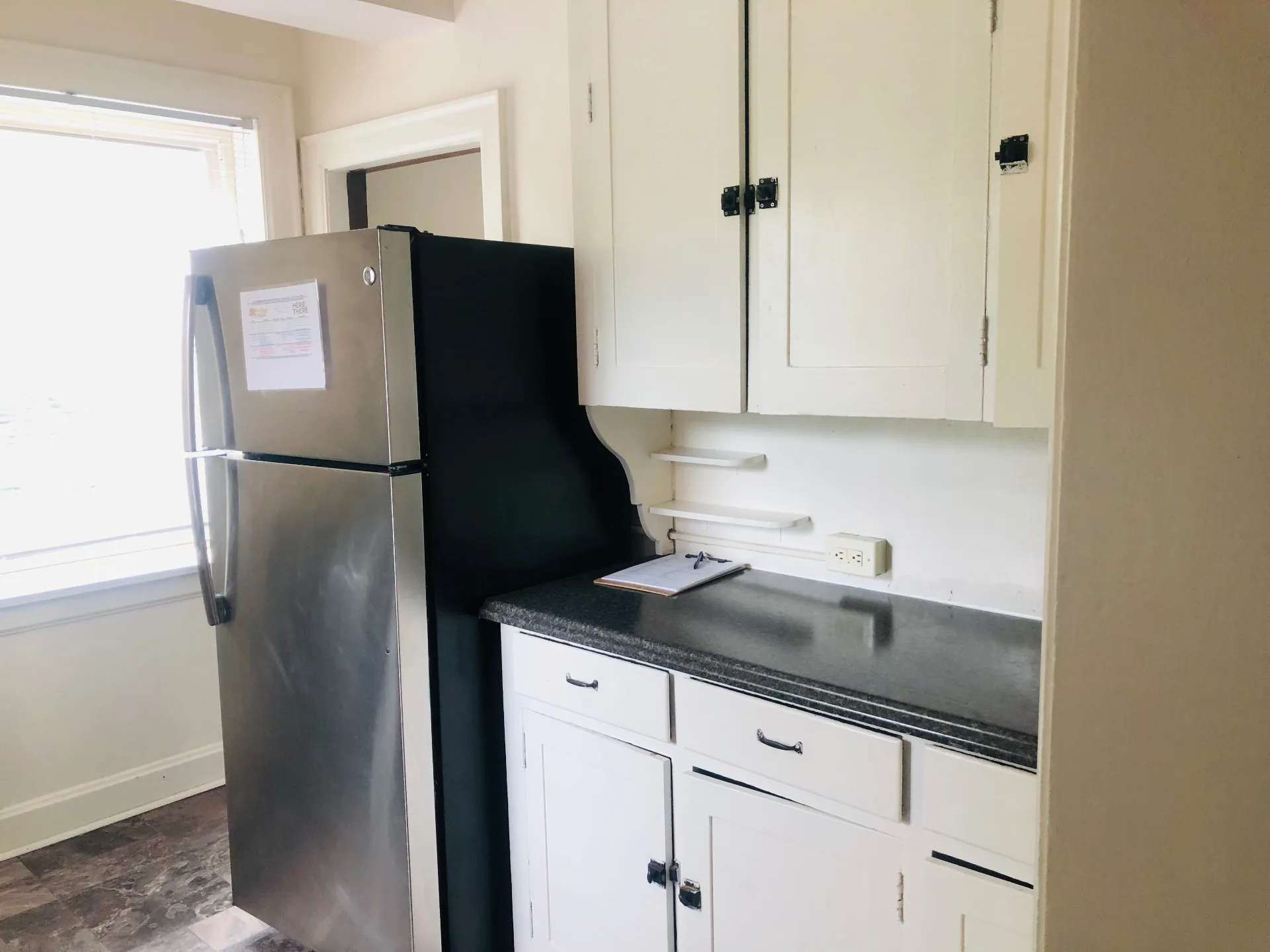 Unit F kitchen with stainless steel refrigerator, white cabinets, and granite countertops